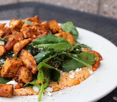 Delicious chicken salad with spinach, feta cheese, and creamy sauce on a white plate.