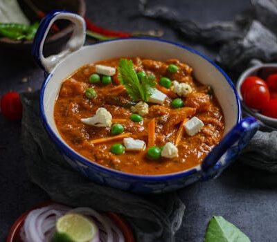Close-up of vibrant Indian mattar paneer curry with fresh ingredients in a ceramic bowl.