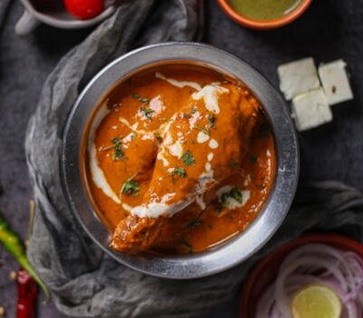 Mouth-watering butter chicken curry garnished with cream and herbs, served in a stainless steel bowl.